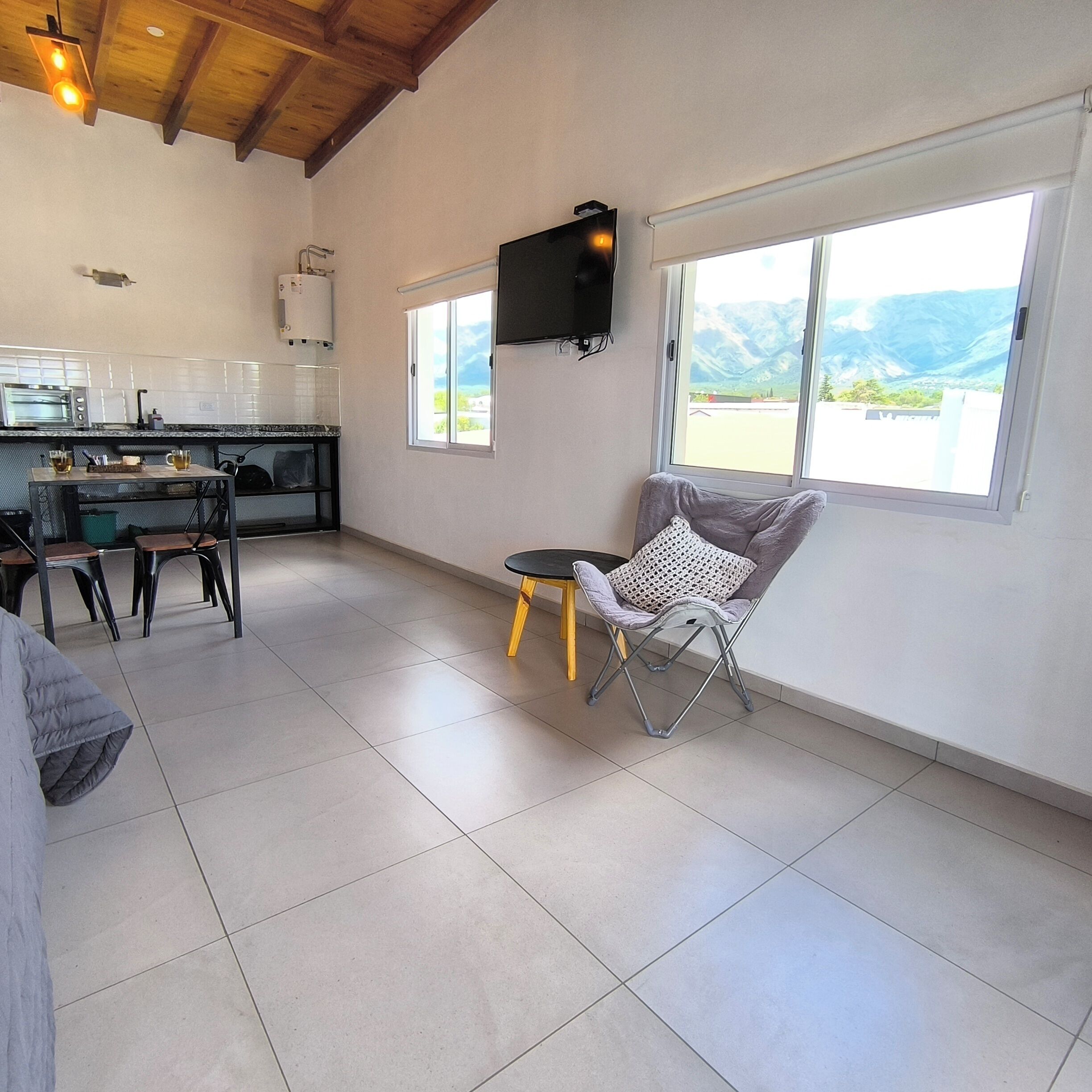 A spacious living area with a kitchen, a dining table, and a comfortable chair.