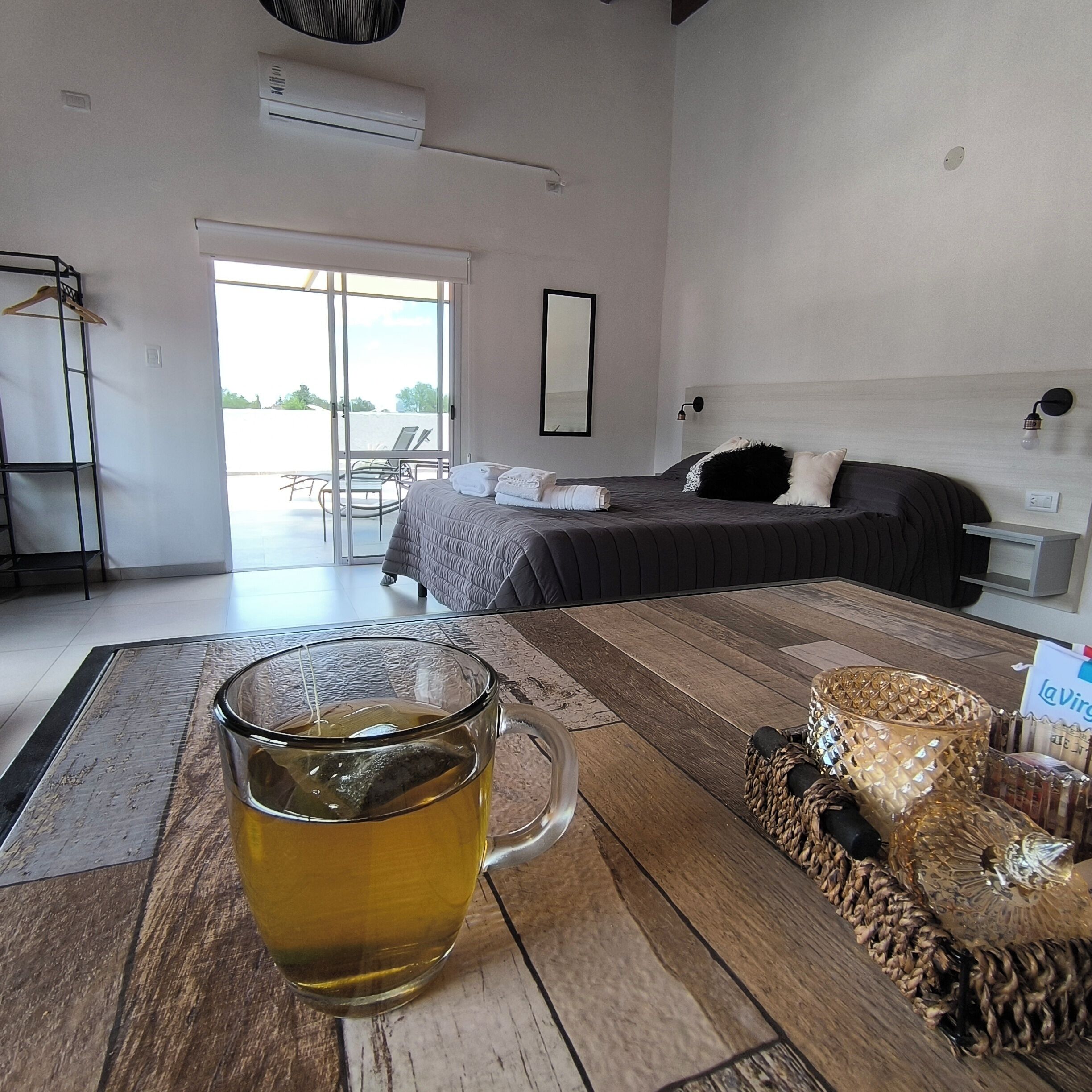 Une chambre d’hôtel avec un lit, une tasse en verre posée sur une table en bois, une chaise et une vue à travers une porte vitrée.