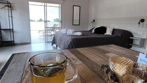 Une chambre d’hôtel avec un lit, une tasse en verre posée sur une table en bois, une chaise et une vue à travers une porte vitrée.