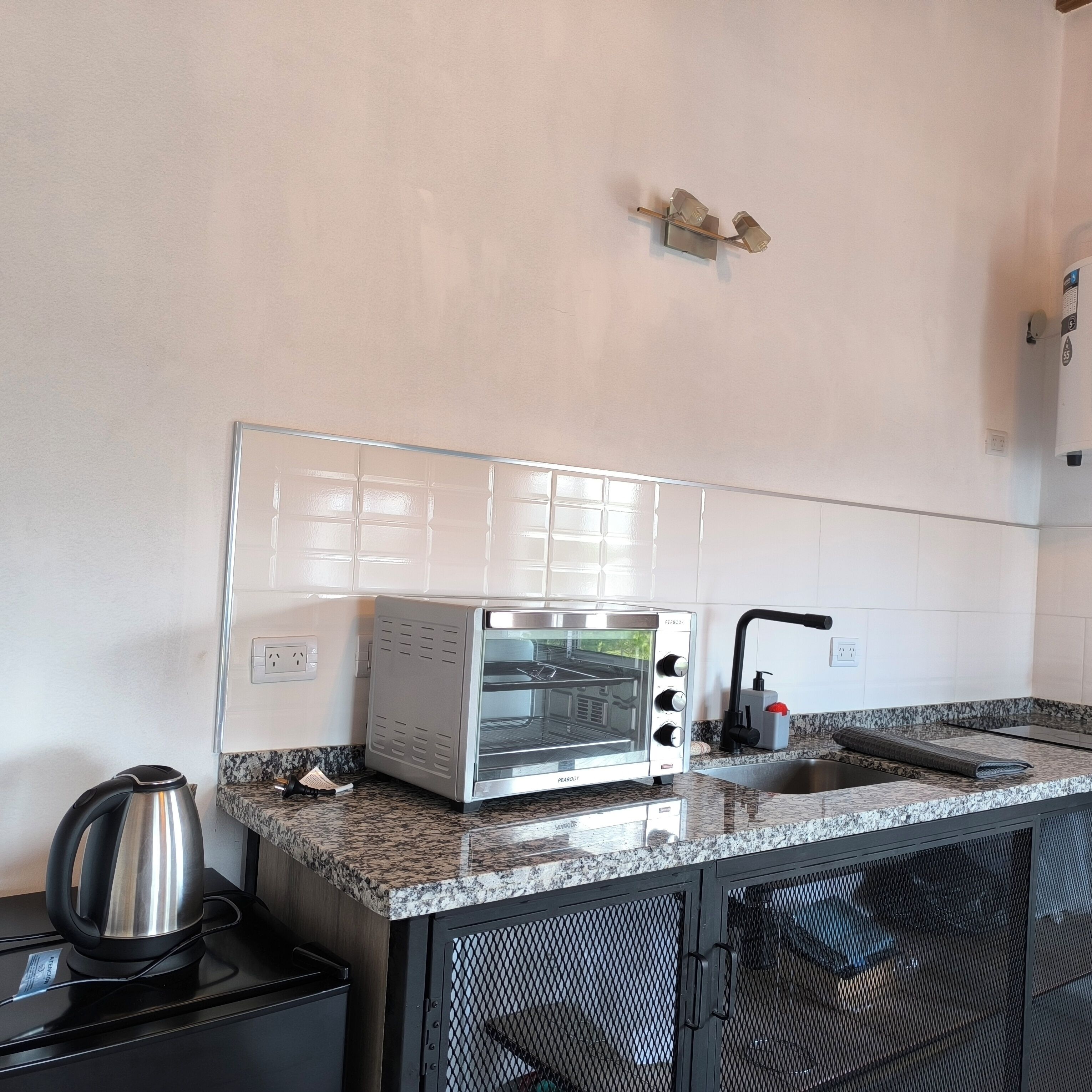 A compact kitchen with a built-in toaster oven, a kettle, and a sink.