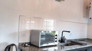A compact kitchen with a built-in toaster oven, a kettle, and a sink.