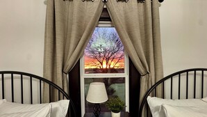 Ein Schlafzimmer mit zwei Betten, einem Nachttisch mit Lampe und Pflanze sowie einem Fenster mit Vorhängen.