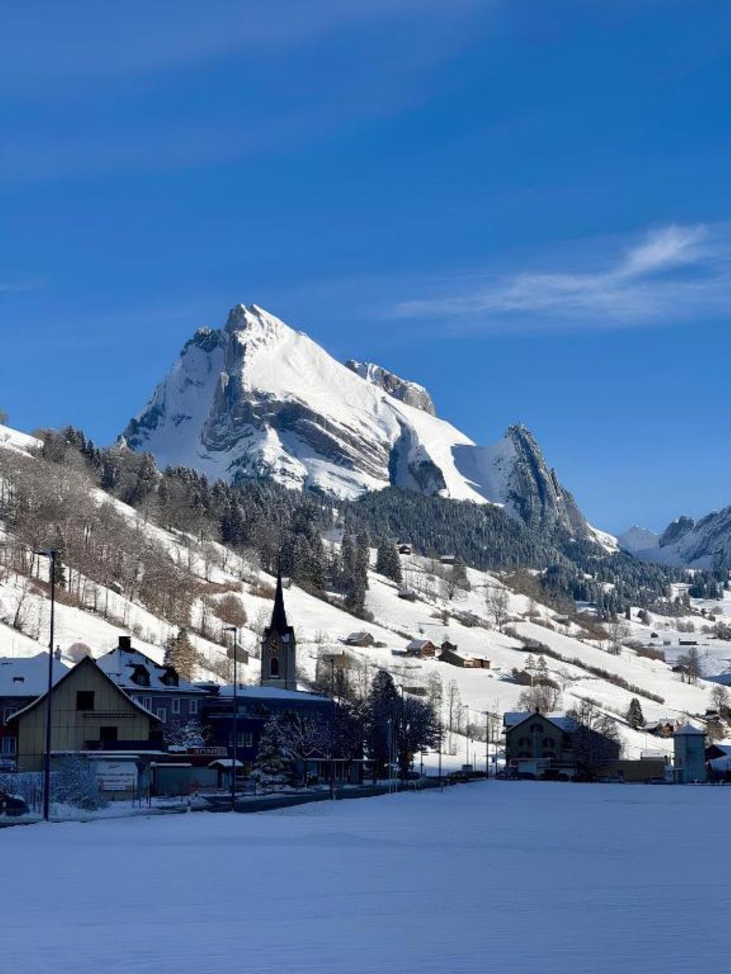 Ein mit Schnee bedeckter Berg, im Vordergrund eine Kirche und Gebäude.