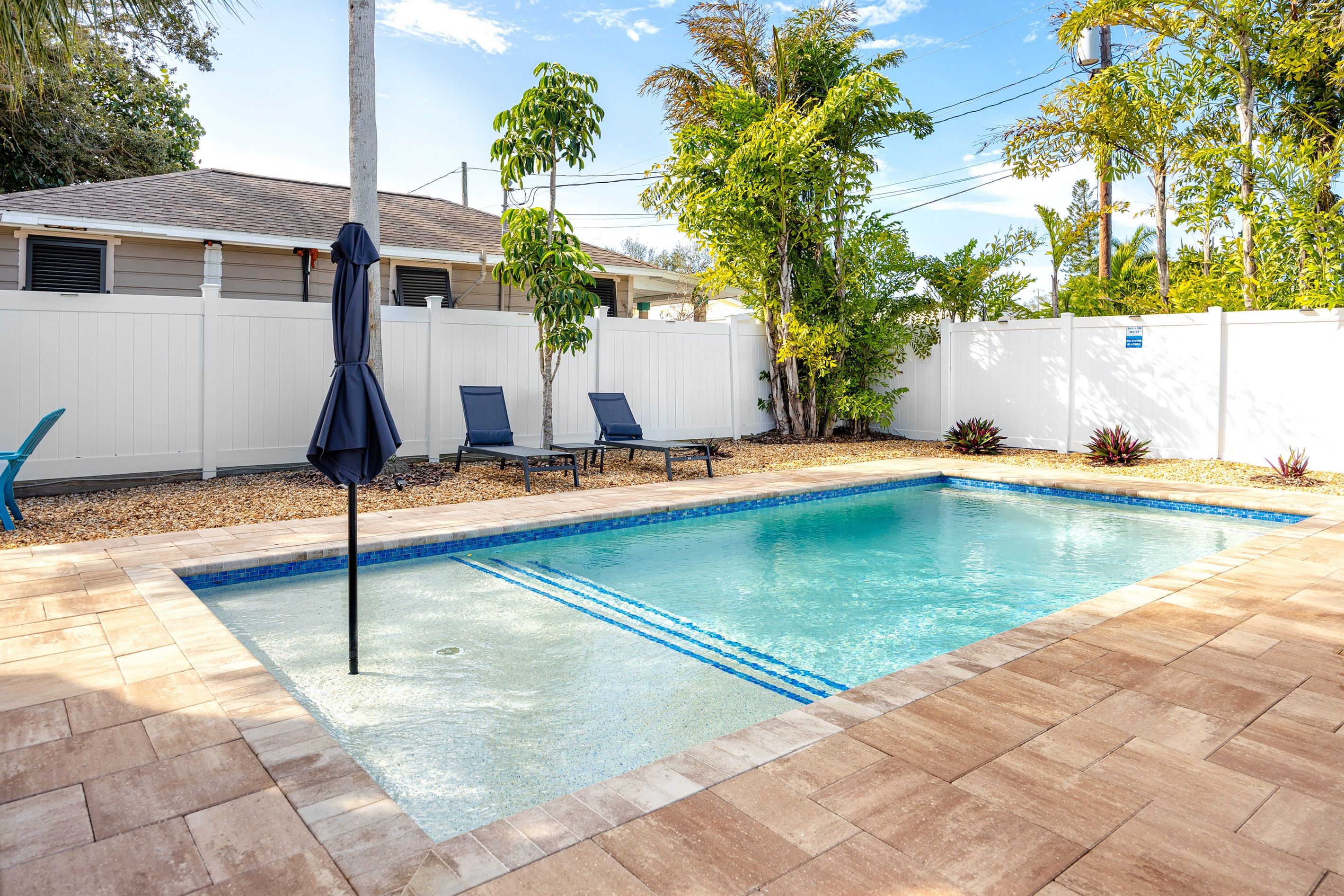 Une piscine avec une terrasse carrelée, des chaises longues et un parasol.