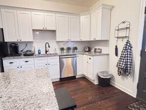 A kitchen with white cabinets, a granite countertop, a dishwasher, and a trash can. - Delta Avenue Oasis: Cozy 2-bedroom, sleeps 5 close to everywhere in Cincinnati (Cincinnati)