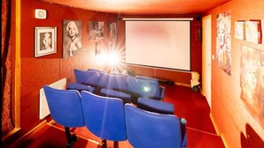 A small cinema room with blue seating, a projection screen, and posters on the walls.