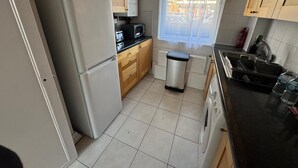 A compact kitchen with a refrigerator, microwave, sink, and a window with a view of parked cars outside. - Central London Apartment Near Tower Bridge | Private Entrance & Garden (London)