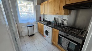 A compact kitchen with wooden cabinets, a washing machine, a gas stove, and a small oven. - Central London Apartment Near Tower Bridge | Private Entrance & Garden (London)