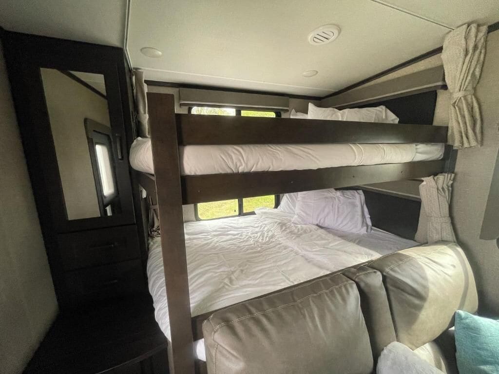 A bunk bed with white bedding, a small table, and a mirror.