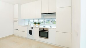 Eine moderne Küche mit weißen Schränken, einer Waschmaschine, einem Backofen und einem Fenster mit Blick auf Grünflächen.