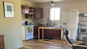 A spacious kitchen with wooden cabinets, a dining table, and a black chair. - Sunny & Private I bedroom House with Sun Room for Guests (Torrey)