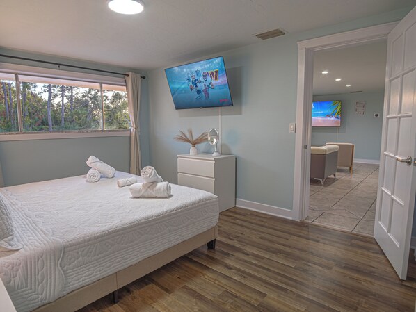 A bedroom with a bed, a TV mounted on the wall, a bedside table with a lamp, and a view of the outdoors through a window. - Delightful 3-bedroom house with Hot tub in Englewood (Englewood)