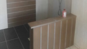 Ein Badezimmer mit Dusche, gefliesten Wänden und einer kleinen Ablage mit einer Flasche.
