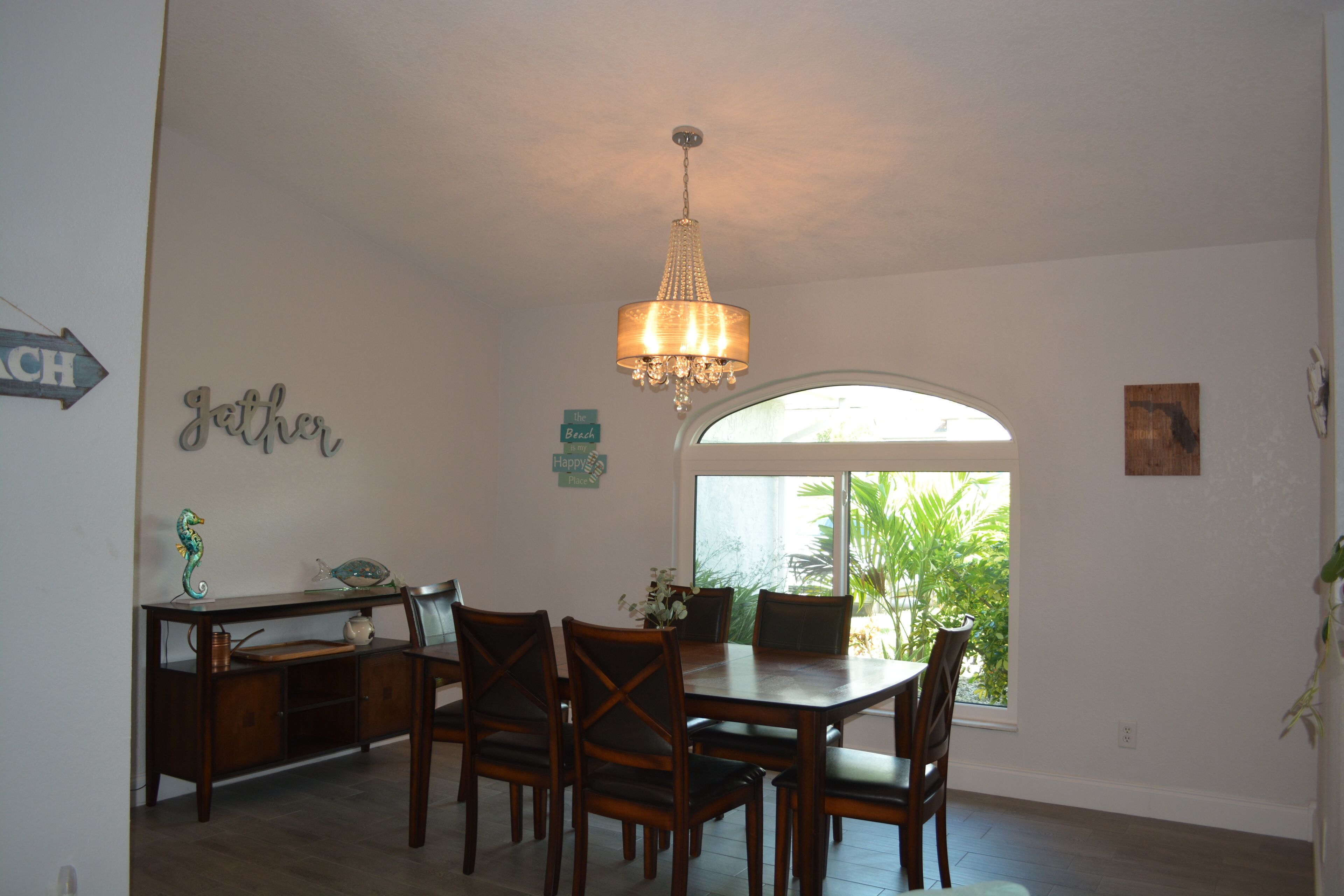 A dining area with a chandelier, wooden table, and chairs. There is a sign on the wall that says "Gather" and another that says "Happy."