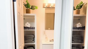 A bathroom with a white sink, mirror, and shelves with towels. There are plants on the shelves and a small cabinet. - Southside City Cottage with ample parking-Sleeps 5 (Jacksonville)