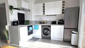 Eine moderne Küche mit weißen Schränken, einer integrierten Waschmaschine, einem Edelstahlkühlschrank und einer kleinen Arbeitsfläche mit einer Kaffeemaschine.
