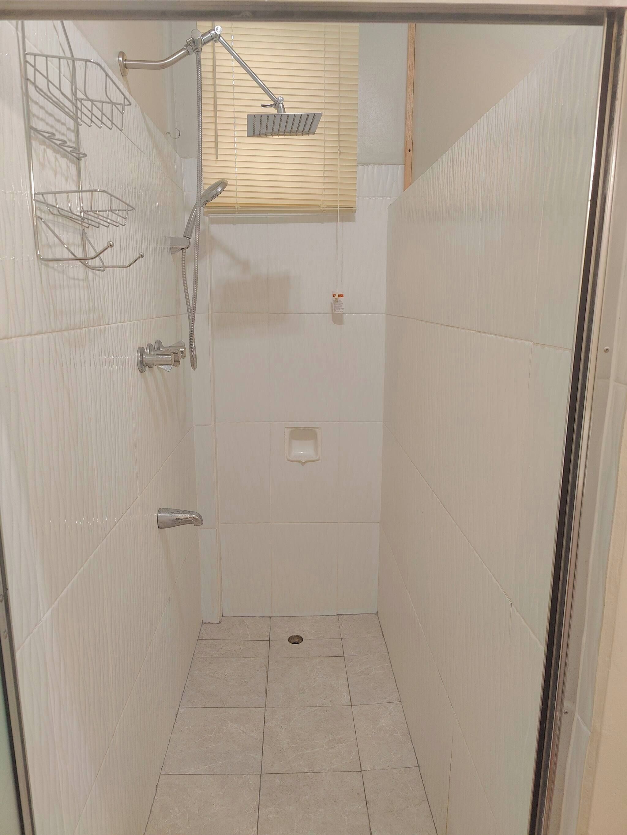 A small, tiled shower room with a handheld showerhead, a wall-mounted faucet, and a toilet.