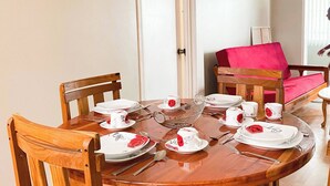 A dining table set with white plates, red napkins, and silverware, surrounded by wooden chairs in a room with a door and a window. - Stylish 1-bed Opposite Queens Park Savannah (Port of Spain)