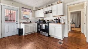 Una cocina con armarios blancos, un horno de acero inoxidable y suelo de madera.