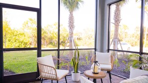 A sunlit patio with wicker chairs and a table, large windows, and a view of palm trees and greenery. - Perfect getaway in SouthWest Florida (Punta Gorda)