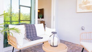 Una sala de estar moderna con un sofá blanco, un sillón de mimbre, una mesa redonda de madera y un florero de vidrio.