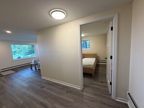 A room with a wooden floor, a bed, a window with a view of trees, and a ceiling light. - Peaceful 3BR paradise on Lake Huron, 100ft shoreline, ideal for a retreat! (Cheboygan)