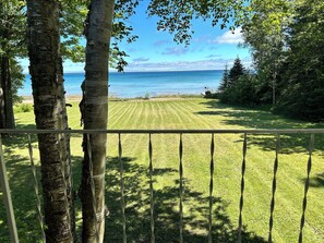 A grassy lawn with a view of a body of water and trees in the background. - Peaceful 3BR paradise on Lake Huron, 100ft shoreline, ideal for a retreat! (Cheboygan)