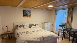 A bedroom with a bed, a bedside table, a chair, a desk, and a window with curtains.