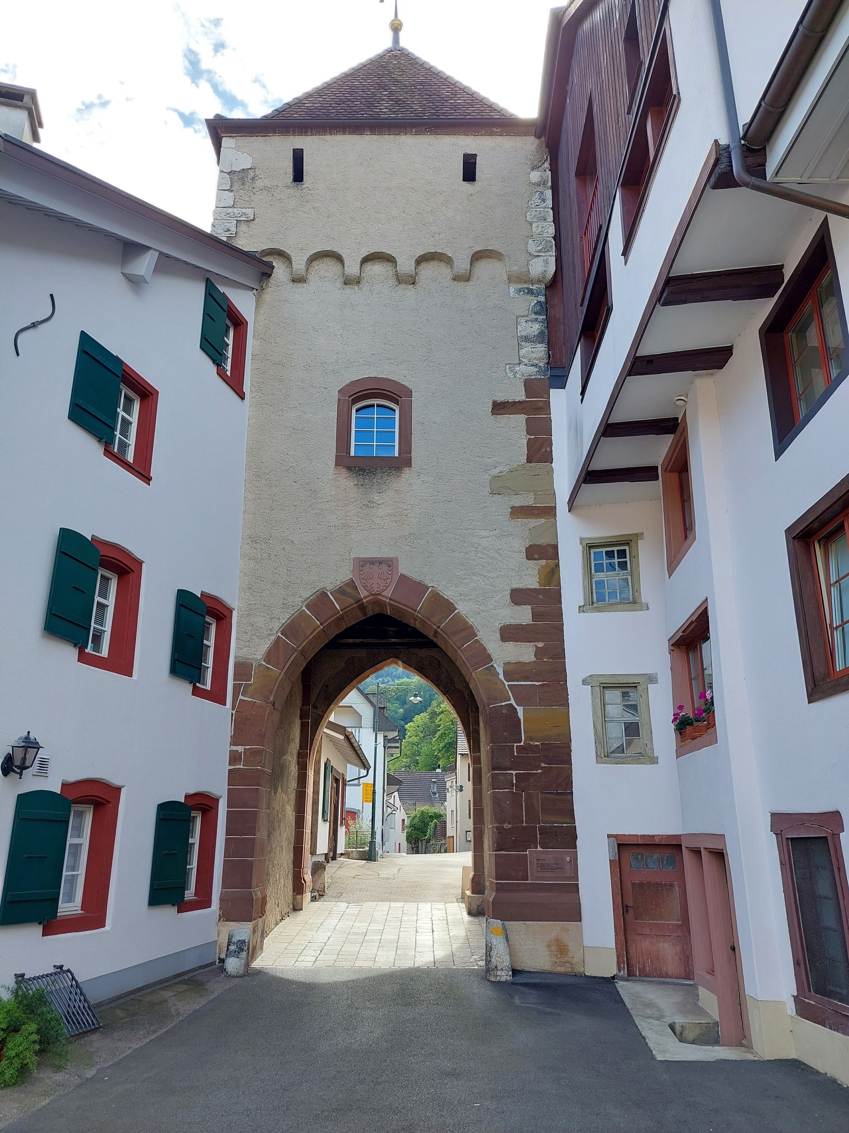 A narrow street with a historic stone archway leading to a building with multiple windows and a small balcony.