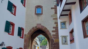 A narrow street with a historic stone archway leading to a building with multiple windows and a small balcony.