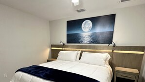 A bedroom with a bed, a nightstand, a wall-mounted painting, and a ceiling fan.