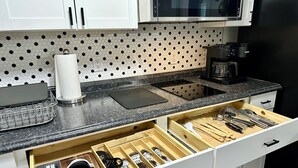 A kitchen with white cabinets, a microwave, a coffee maker, and a drawer organizer with utensils.
