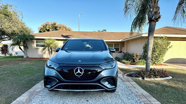 A Mercedes-Benz parked on a gravel driveway in front of a house with a well-maintained lawn and palm trees.