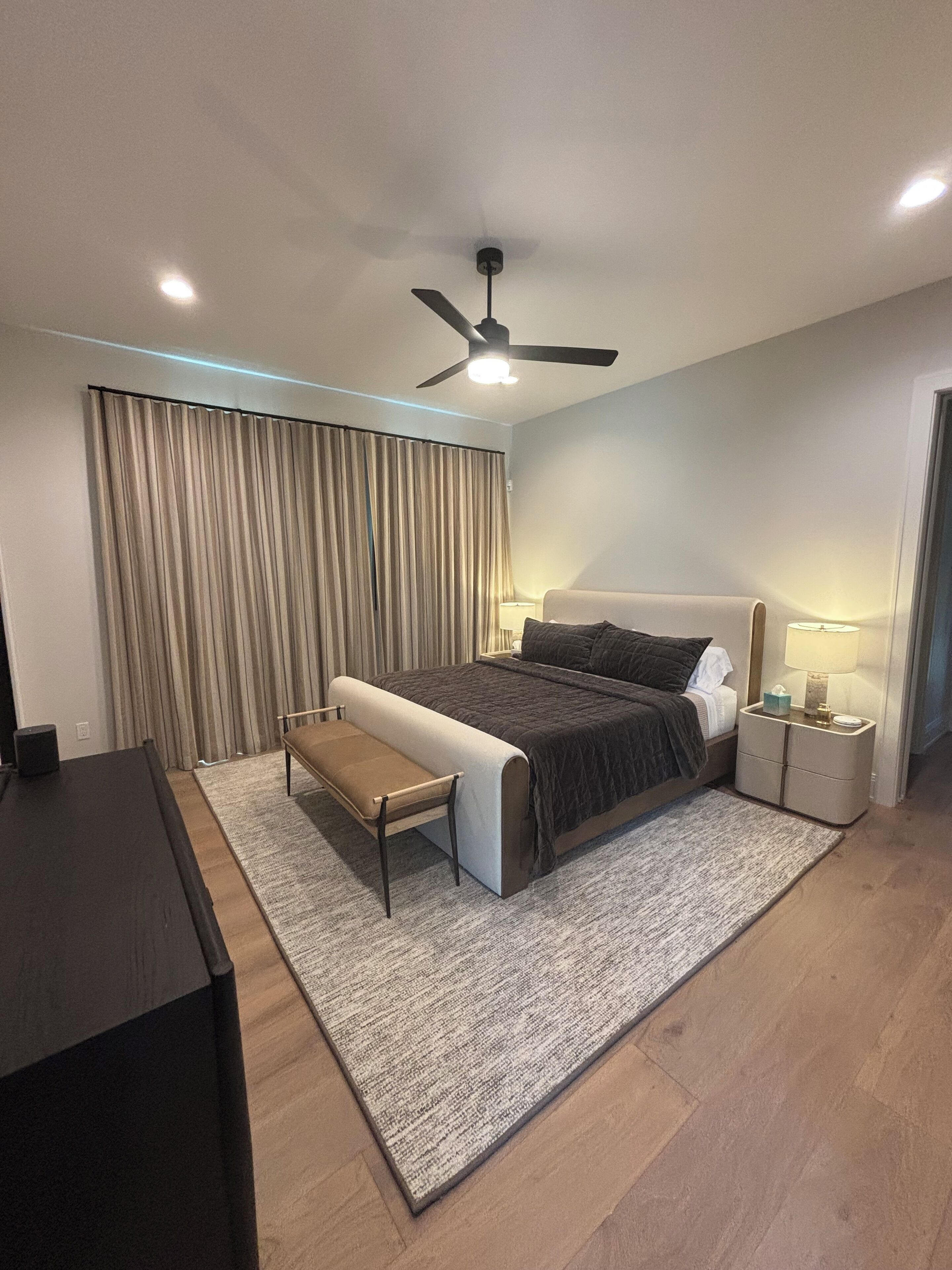 A modern bedroom with a bed, bedside tables, a desk, and a ceiling fan.