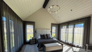 Une chambre à coucher moderne avec un grand lit, une table de chevet, un banc et une vue sur l’extérieur.