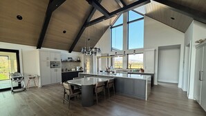 Une cuisine spacieuse dotée d’un grand îlot central, de poutres en bois et offrant une vue sur l’extérieur.
