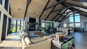 Un vaste espace de vie comprenant un grand canapé, une table à manger et des chaises, une cheminée et de grandes fenêtres donnant sur l’extérieur.