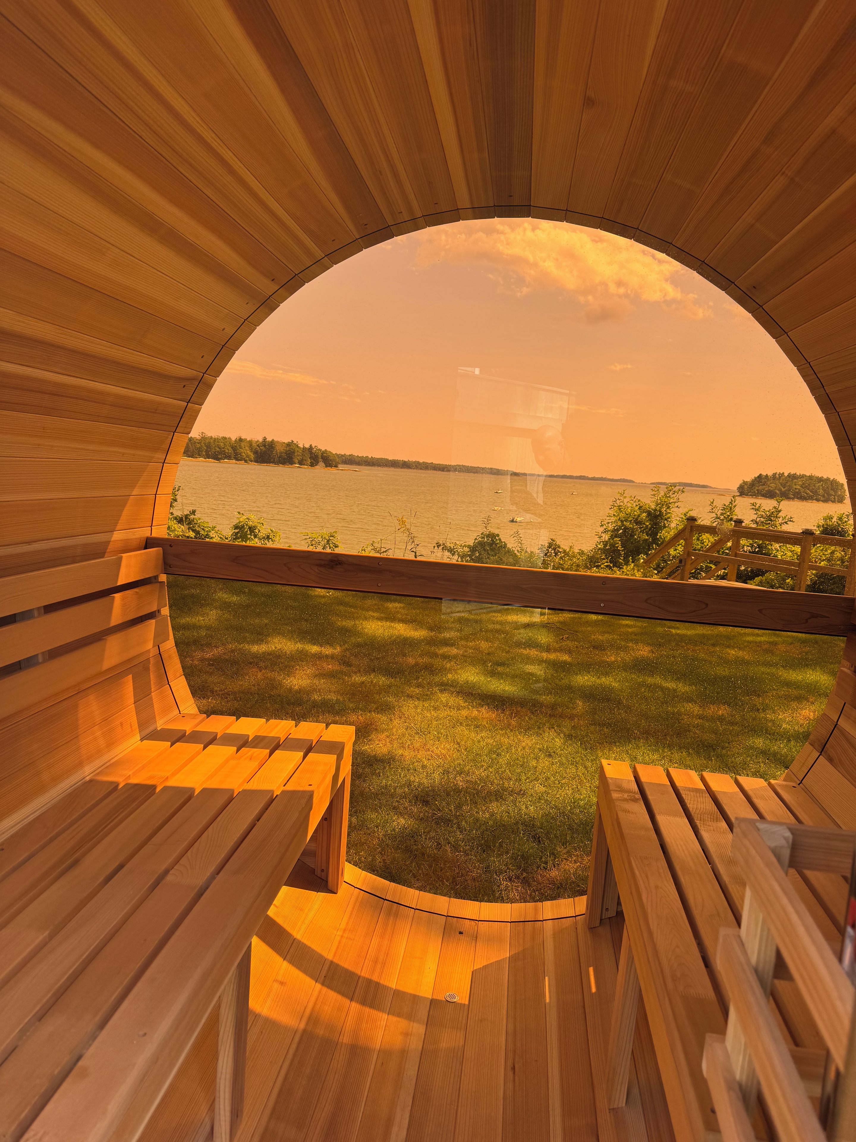 A circular wooden structure with benches facing a body of water and a grassy area.