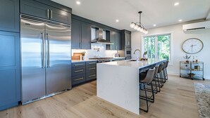 Een moderne keuken met een groot eiland, roestvrijstalen apparatuur en uitzicht op het groen.