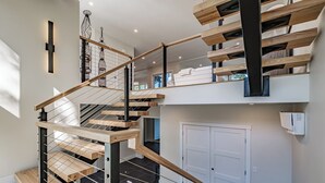 Een moderne trap met houten treden en metalen leuningen, die naar een tweede verdieping leidt met uitzicht op het buitengebied.