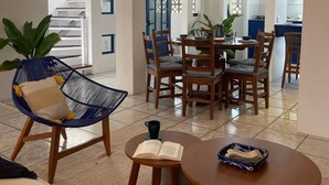 A spacious living area with a dining table, chairs, and a blue chair with a cushion. There is a sofa, a coffee table, and a plant. - Crete Apartment, A Mediterranean charm. (Puerto Vallarta)
