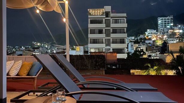 A rooftop terrace with lounge chairs and a table, overlooking a cityscape at night. - Crete Apartment, A Mediterranean charm. (Puerto Vallarta)