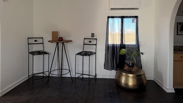 Ein Zimmer mit zwei schwarzen Metallstühlen, einem kleinen runden Tisch und einem dekorativen Goldtopf auf einem Tisch.