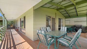 A covered outdoor patio with a wooden deck, a table with chairs, and a grill area.