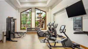 Un gimnasio con máquinas de cardio, pesas libres y un televisor en la pared.