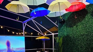 An outdoor seating area with wicker furniture, a pool, and a large screen displaying a movie.