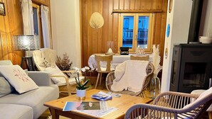 Ein gemütliches Wohnzimmer mit Holzbalkendecke, Kamin und Essbereich mit Tisch und Stühlen.