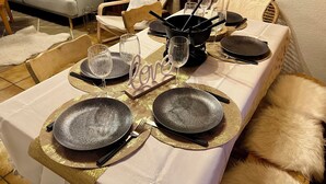 Ein Esstisch ist gedeckt mit Tellern, Besteck und Gläsern, umgeben von einer gemütlichen Wohnbereits mit einer Couch und dekorativen Kissen.
