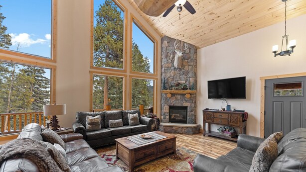 A spacious living room with leather sofas, a stone fireplace, large windows, and a ceiling fan. - 14mcbr3 (Breckenridge)
