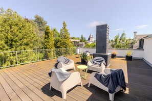 Terraza en la azotea con mobiliario exterior, una chimenea y abundante vegetación.